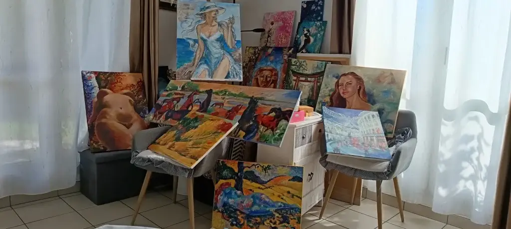 Vue d’ensemble de l’atelier de Delia Teo baigné de lumière naturelle, toiles posées sur des chaises et un meuble devant les voilages
